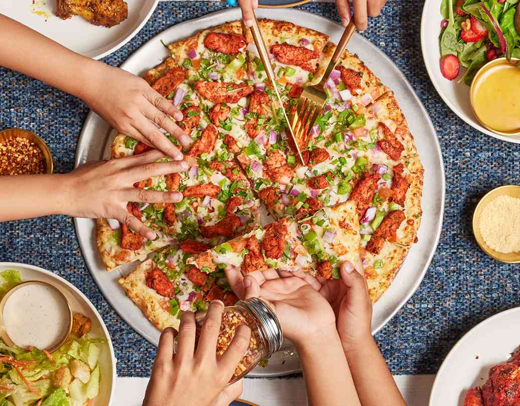 Image of hand picking up slices from a large Tandoori Pizza in Richmond Hill